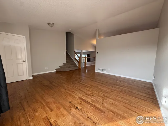 a view of an empty room with stairs and a wooden floor