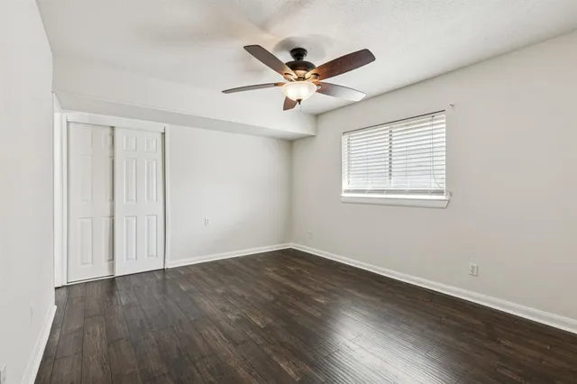 an empty room with wooden floor fan and windows
