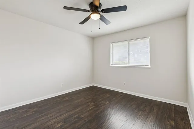 an empty room with wooden floor ceiling fan and windows