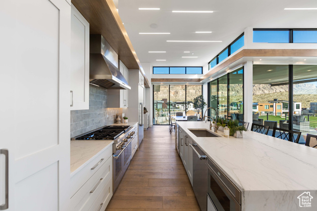 3558 South Cypress Road Hurricane, UT 84737 - Photo 8 of 57 Kitchen with white cabinets, light stone countertops, dark hardwood / wood-style floors, wall chimney range hood, and stainless steel appliances