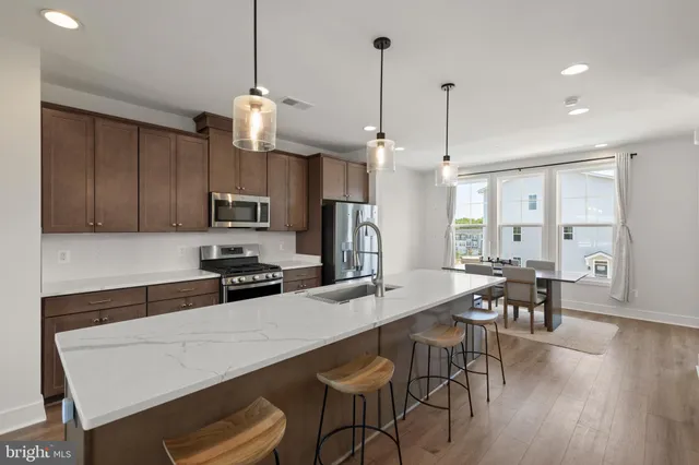 a kitchen with stainless steel appliances granite countertop a stove a refrigerator a kitchen island a dining table and chairs with wooden floor