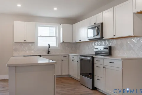 a kitchen with white cabinets appliances a sink and a window
