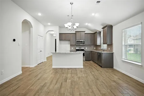 a large kitchen with granite countertop a stove a sink dishwasher a refrigerator white cabinets and wooden floor