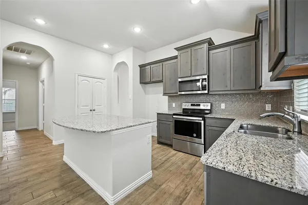 a kitchen with stainless steel appliances granite countertop a stove top oven a sink and dishwasher a refrigerator with wooden floor