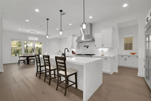 a kitchen with stainless steel appliances kitchen island granite countertop a stove a sink a dining table and chairs with wooden floor
