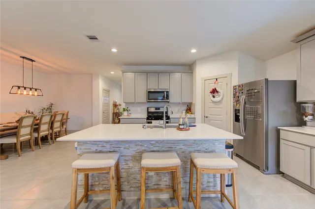a kitchen with stainless steel appliances granite countertop a dining table chairs refrigerator and microwave