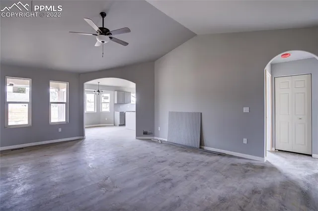an empty room with chandelier fan and windows