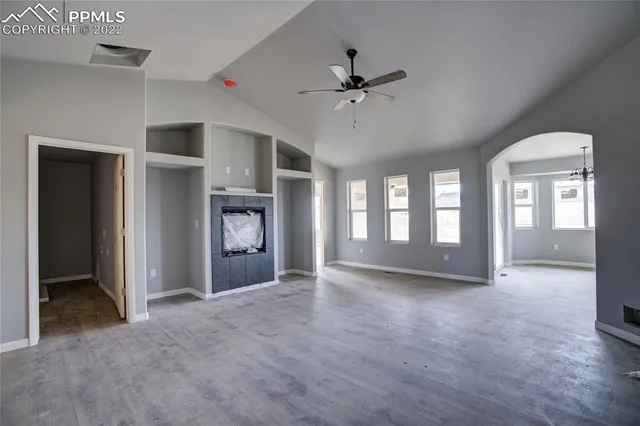 a view of an empty room with chandelier fan and windows