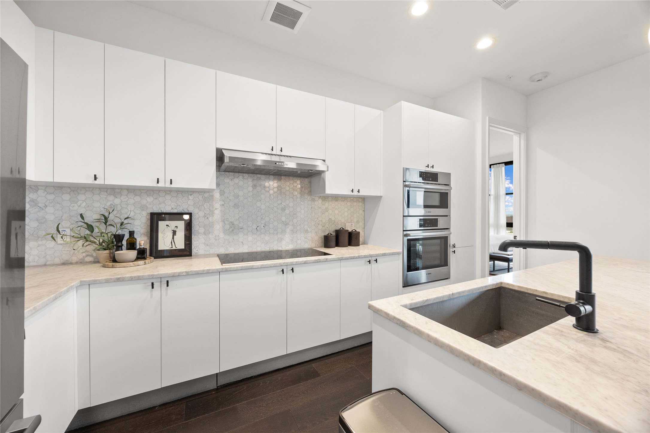 800 Embassy Drive, Unit 602 Austin, TX 78702 - Photo 11 of 37 Contemporary kitchen with white cabinetry, light stone countertops, stainless steel appliances, a honeycomb tile backsplash, and dark wood-finish flooring