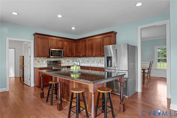 a kitchen with stainless steel appliances granite countertop a refrigerator a stove top oven a sink dishwasher and white cabinets with wooden floor