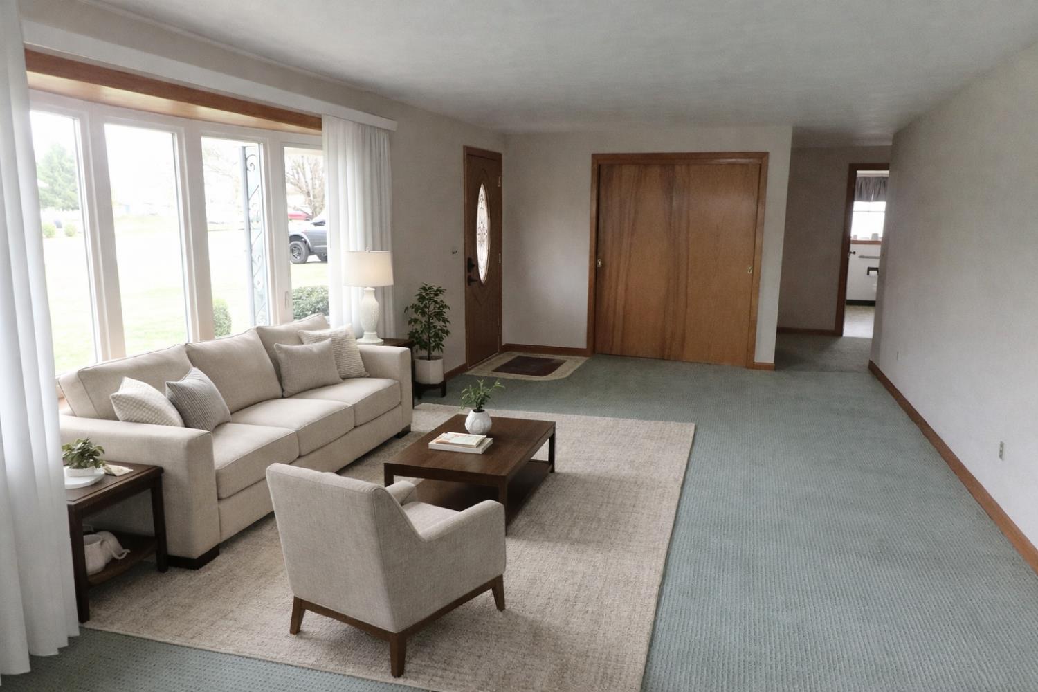 315 Nieman Street Sunman, IN 47041 - Photo 2 of 30 Bright and spacious living room featuring large front-facing windows that fill the space with natural light. The open layout offers flexible furniture arrangement options and easy flow to adjacent areas, making it ideal for both everyday living and entertaining. Note: This image has been virtually staged to illustrate potential furniture placement and design possibilities.