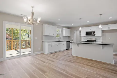 a kitchen with stainless steel appliances granite countertop a refrigerator a sink dishwasher a stove and white cabinets with wooden floor