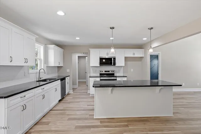 a large kitchen with stainless steel appliances granite countertop a stove top oven a sink dishwasher and a refrigerator with wooden floor