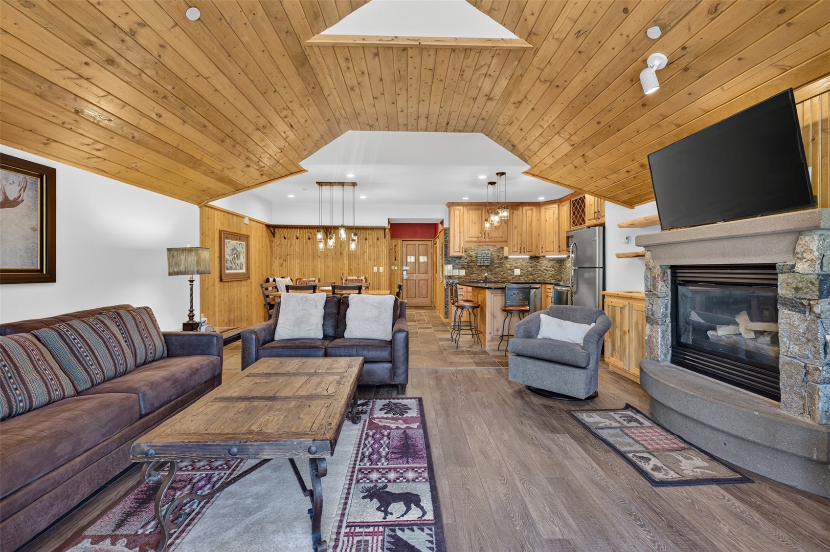 Vaulted wood-paneled ceiling, stone fireplace with a stone hearth, wood-finish flooring, and natural wood cabinetry