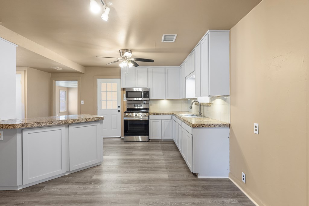 1200 North Street Kerrville, TX 78028 - Photo 15 of 50 a large kitchen with granite countertop a stove top oven a sink dishwasher and a refrigerator with wooden floor