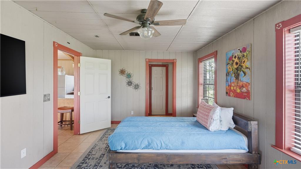127 Offer Llano, TX 78643 - Photo 21 of 40 Room featuring light-colored vertical paneling, a ceiling fan with light fixture, two windows with blinds and accent trim, and a doorway with accent trim