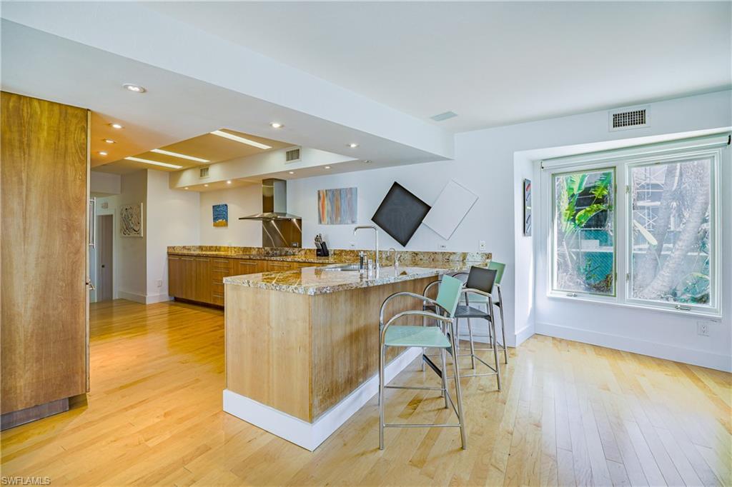 536 Turtle Hatch Road Naples, FL 34103 - Photo 10 of 28 Kitchen featuring light stone countertops, a peninsula, recessed lighting, a breakfast bar, and wall chimney exhaust hood