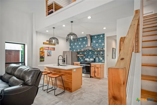 a living room with stainless steel appliances furniture a rug and a view of kitchen
