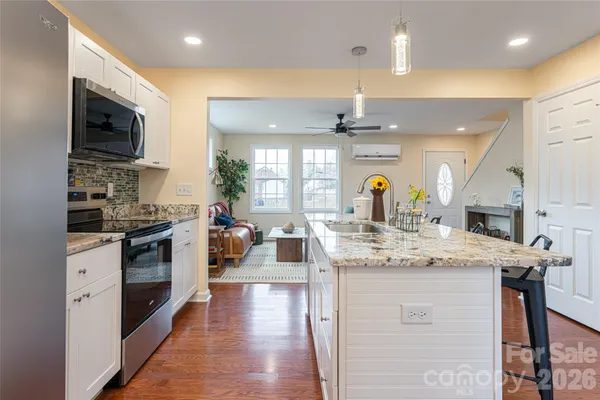 a kitchen with stainless steel appliances kitchen island granite countertop a stove top oven a sink a dining table and chairs with wooden floor