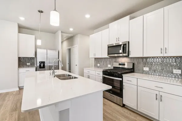 a kitchen with kitchen island a stove a sink a refrigerator and white cabinets with wooden floor