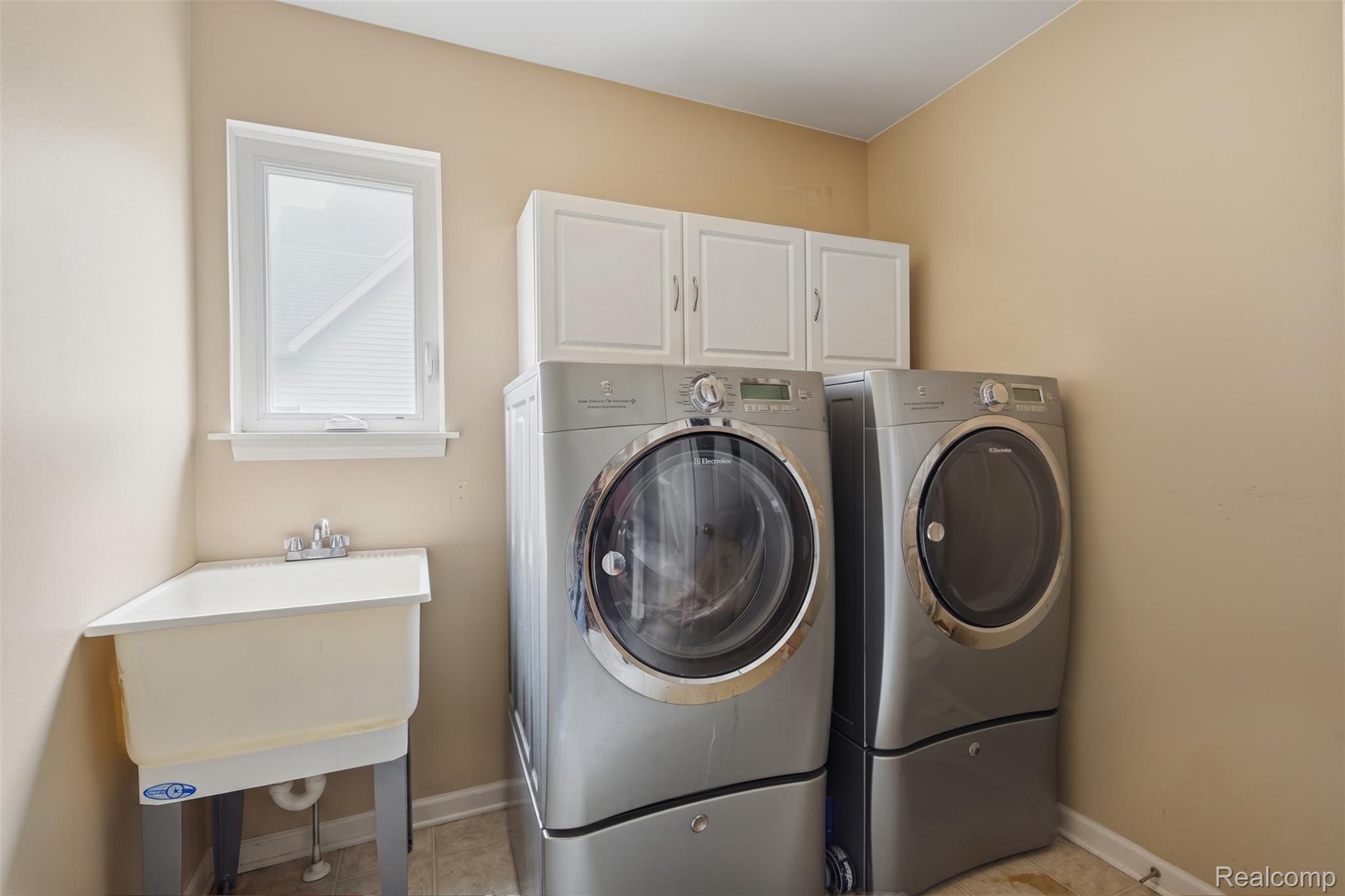 170 Fairhill Way Howell, MI 48843 - Photo 25 of 46 Utility space featuring a laundry sink, window, white upper cabinetry, and tile-look flooring