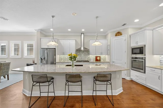 a kitchen with stainless steel appliances kitchen island granite countertop a dining table chairs refrigerator and microwave