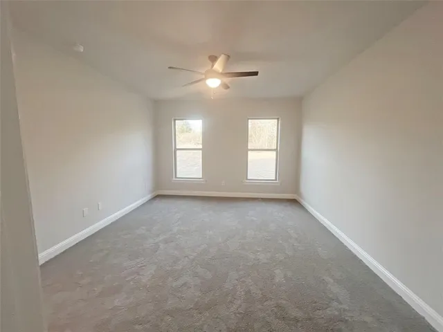 an empty room with chandelier fan and windows