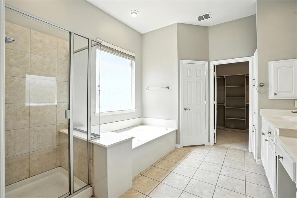 8220 Holliday Road Lantana, TX 76226 - Photo 22 of 40 Spacious bathroom featuring a glass-enclosed shower with tiled walls and built-in bench, a separate soaking tub with a window, white cabinetry with integrated sinks, and tiled flooring