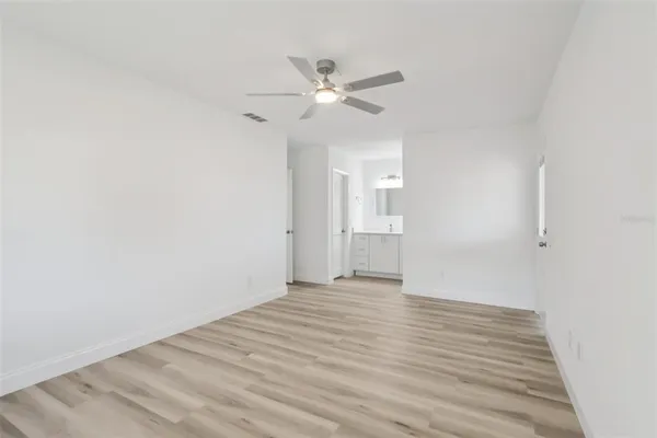 a view of an empty room with wooden floor and a ceiling fan