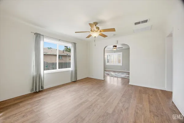 an empty room with wooden floor chandelier fan and windows
