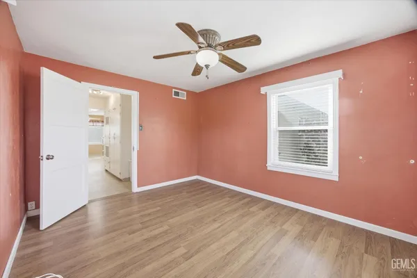 a view of an empty room with wooden floor and a ceiling fan