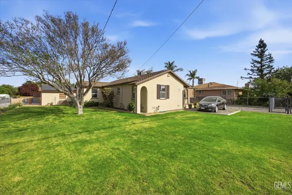 a view of a white house in front of a big yard with large trees