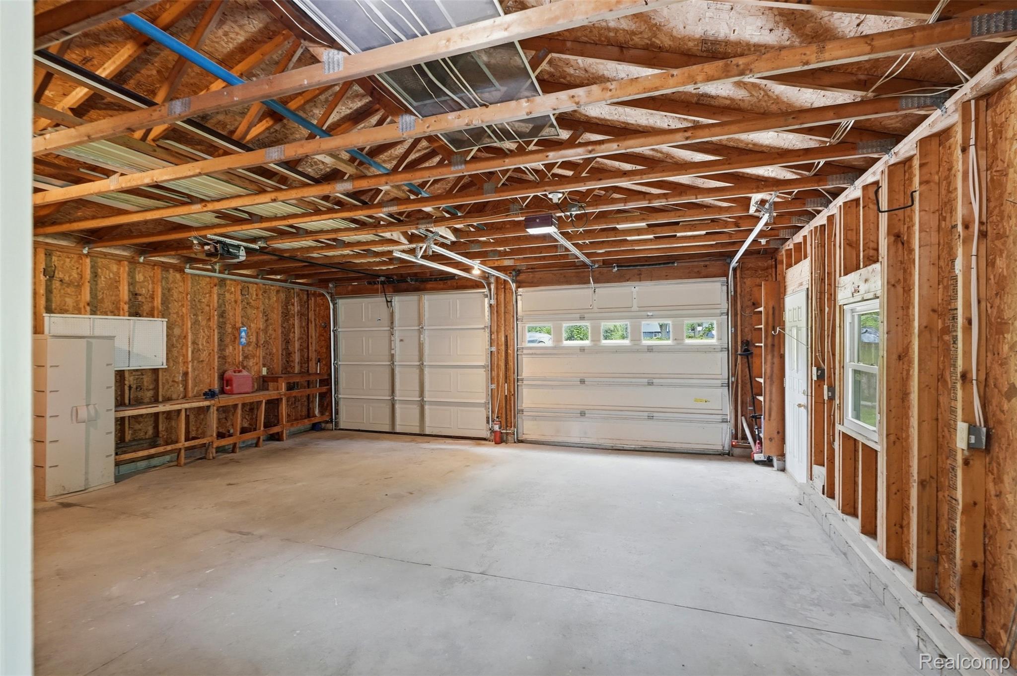 4420 Dublin Road Burton, MI 48529 - Photo 33 of 56 Spacious garage with exposed wood framing, two white paneled overhead doors, and a built-in workbench with cabinetry