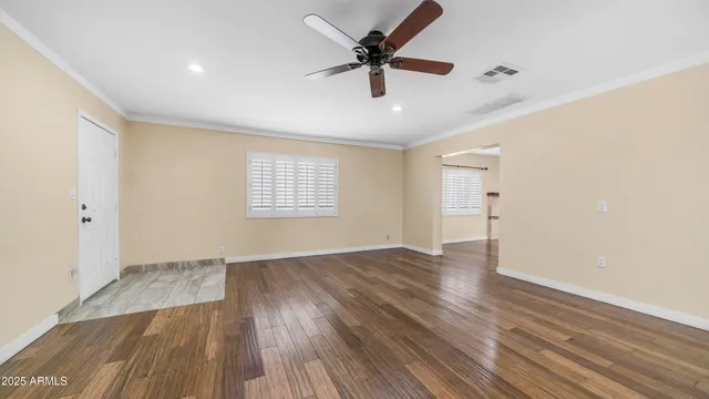 an empty room with wooden floor ceiling fan and windows