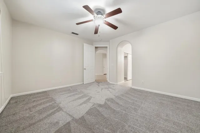an empty room with chandelier fan and windows