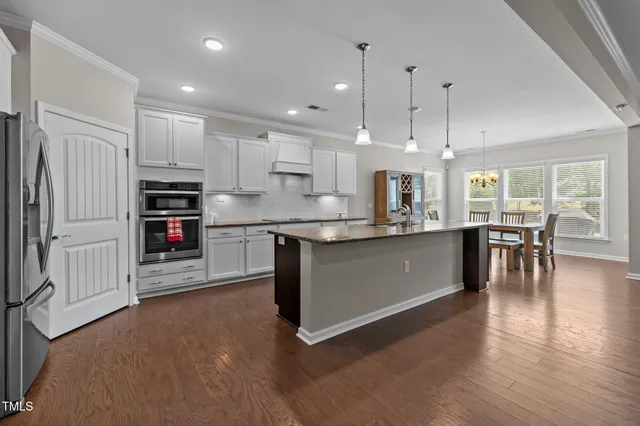 a large kitchen with stainless steel appliances granite countertop a stove a sink a refrigerator and a dining table with wooden floor