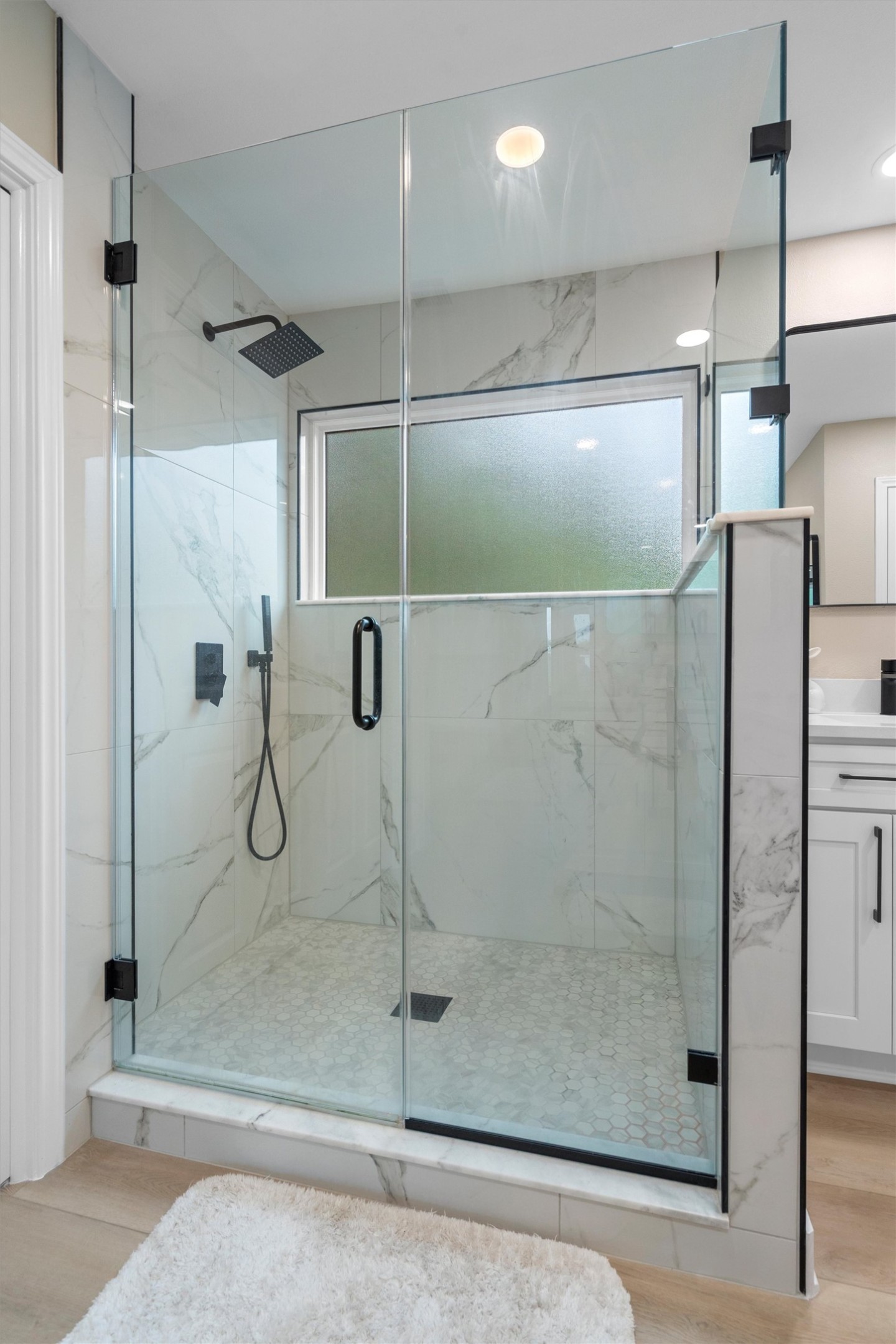 307 Hurst Creek Road Austin, TX 78734 - Photo 31 of 40 Spacious glass-enclosed shower featuring large format white tile walls with grey veining, a hexagonal tile floor, matte black fixtures, and an integrated frosted window