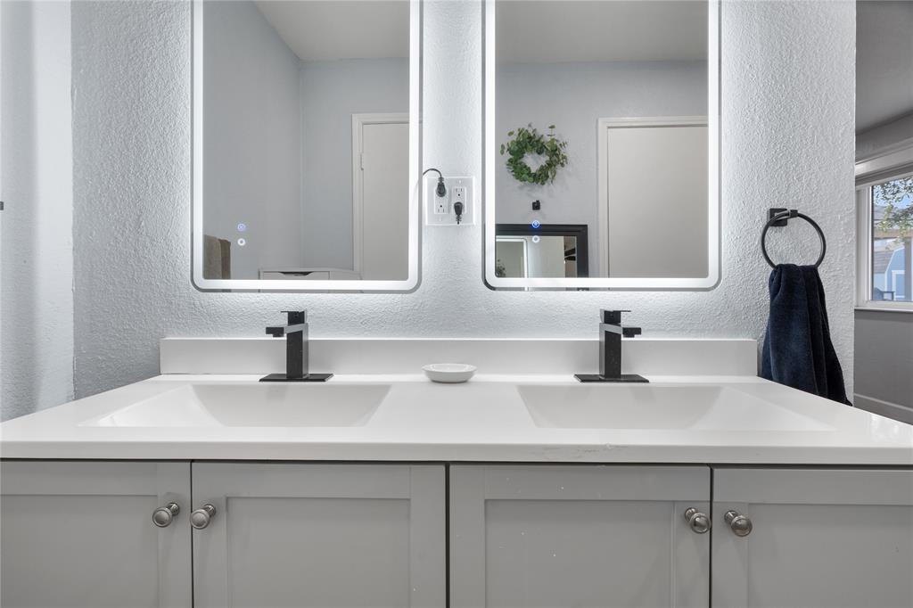 7629 Cedarhill Road Watauga, TX 76148 - Photo 25 of 26 Dual integrated sinks with a white countertop and matte black faucets, complemented by two illuminated vanity mirrors