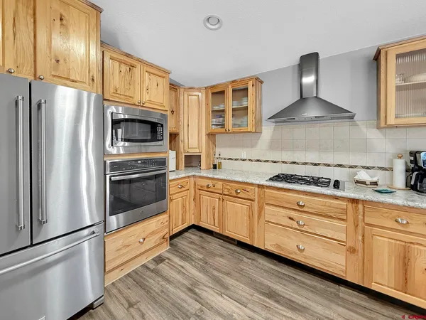 a kitchen with stainless steel appliances granite countertop a refrigerator a sink dishwasher a stove and a dining table with wooden floor