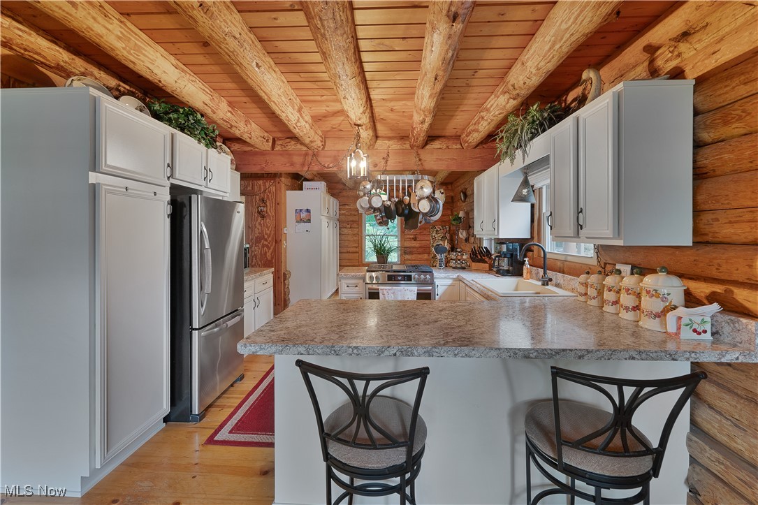 14 Clingan Road Struthers, OH 44471 - Photo 16 of 50 Kitchen with rustic walls, a peninsula, appliances with stainless steel finishes, white cabinets, and a wood ceiling with exposed beams