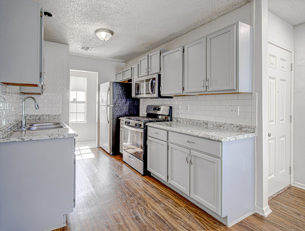 7908 West Gate Boulevard, Unit B Austin, TX 78745 - Photo 11 of 23 Kitchen with stainless steel appliances, a textured ceiling, light wood-style floors, gray cabinetry, and decorative backsplash