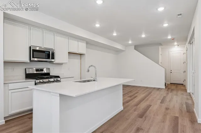 a kitchen with stainless steel appliances a microwave a sink a stove a microwave a refrigerator cabinets and wooden floor