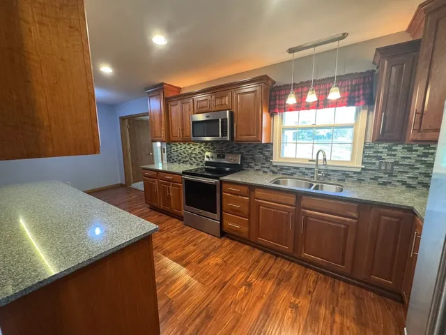 a kitchen with stainless steel appliances granite countertop a sink a stove and a wooden cabinets