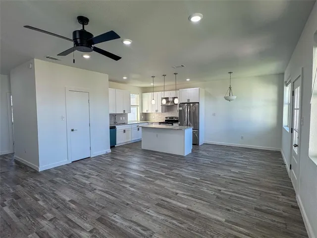 a view of an empty room and kitchen view with wooden floor