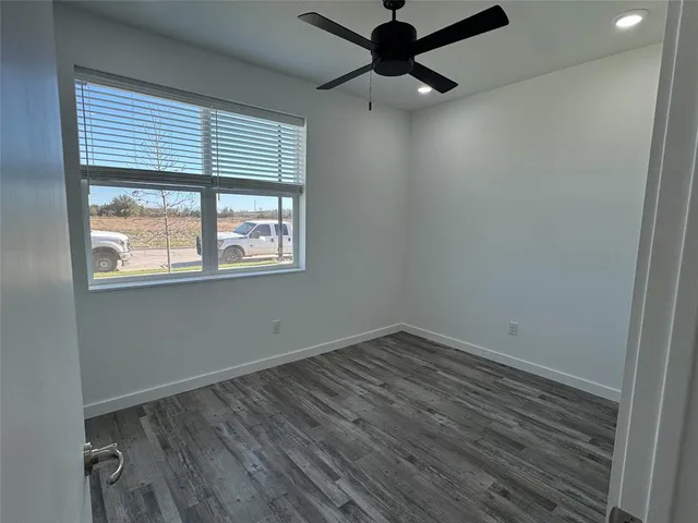 an empty room with wooden floor fan and windows