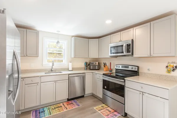 a kitchen with stainless steel appliances granite countertop a sink a stove a microwave a refrigerator a window and cabinets