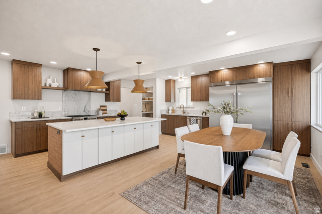 1168 East Center Street Bountiful, UT 84010 - Photo 7 of 38 Open-concept kitchen featuring wood-finish cabinetry, a large center island with a light-toned countertop, stainless steel appliances, a range with a marble-patterned backsplash, and recessed lighting