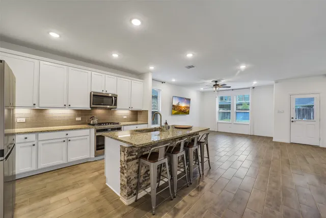 a kitchen with stainless steel appliances granite countertop a stove top oven a sink dishwasher a dining table and chairs with wooden floor