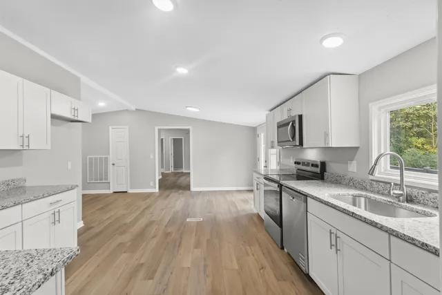 a kitchen with granite countertop a sink cabinets wooden floor and stainless steel appliances