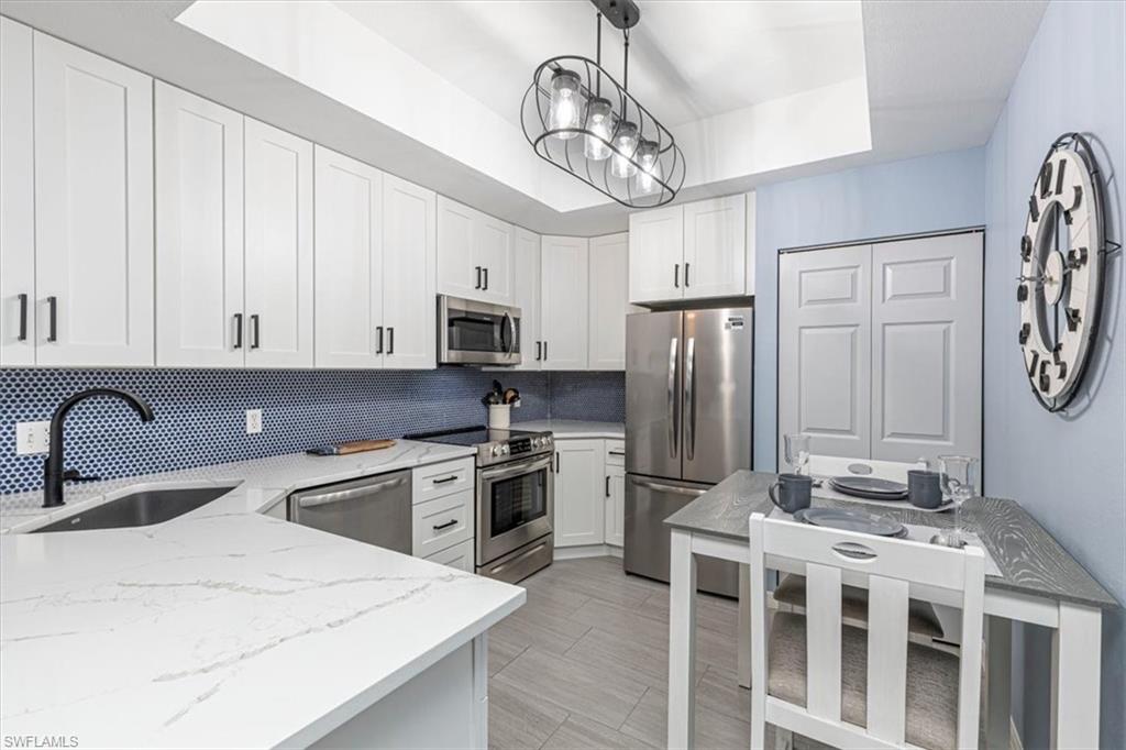 809 Augusta Boulevard, Unit 3 Naples, FL 34113 - Photo 1 of 32 Kitchen featuring a raised ceiling, appliances with stainless steel finishes, white cabinets, and light stone countertops